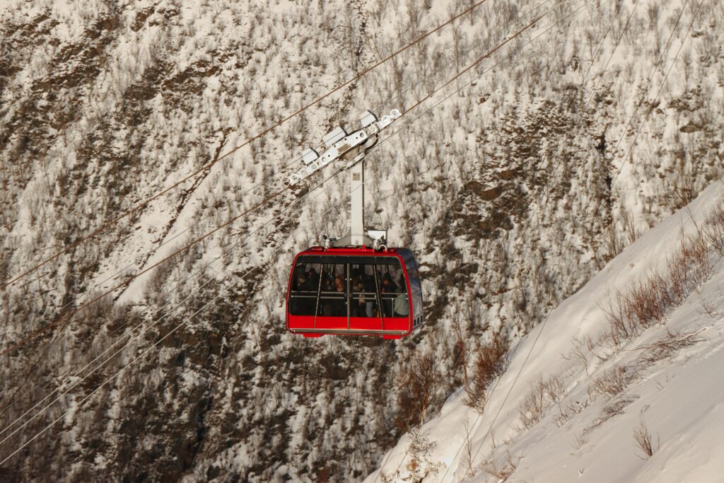 A vibrant red cable car traverses a snowy landscape in Tromsø, Norway, capturing winter adventure.