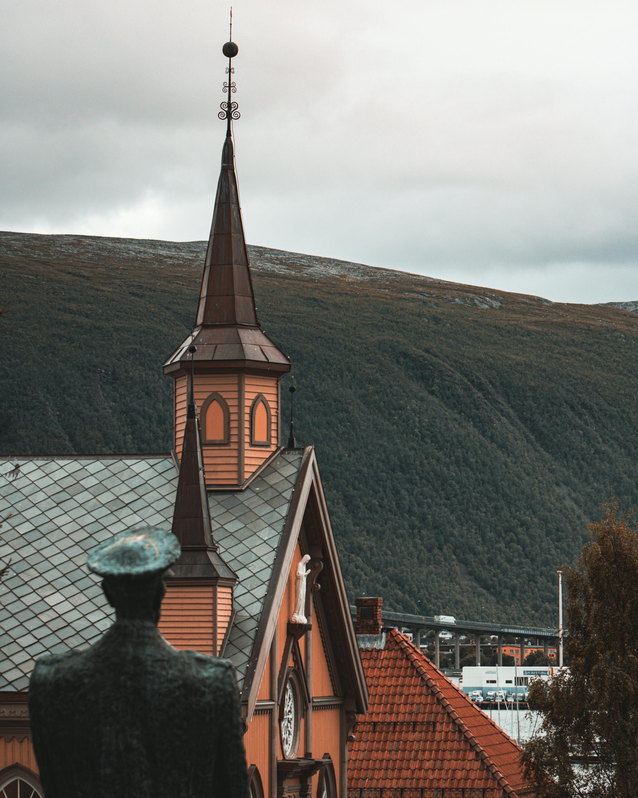 Scenic view of a Gothic church tower in Tromsø, with mountainous backdrop.